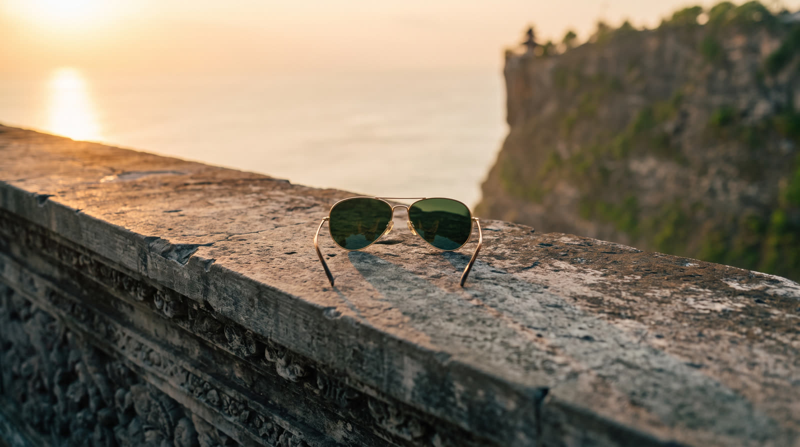 Gold aviator sunglasses lying on the stone wall above the ocean
